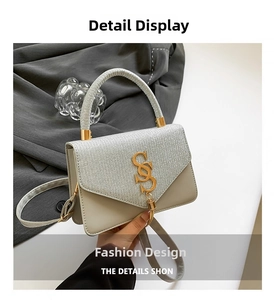 Detail of silver textured fabric shoulder bag with golden logo and tassel charm
