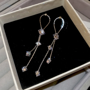 Gros plan de boucles d'oreilles à pompons longs avec zircons carrés et chaîne dorée