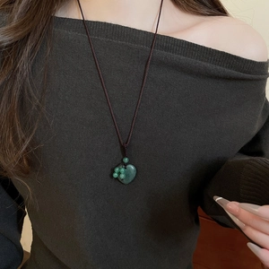 Detailed view of a green heart stone pendant necklace on a braided cord worn by a model