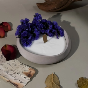 Detalle de vela de soja con flores secas violetas y mecha de madera en cuenco gris