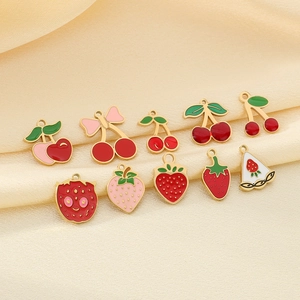 Ciondoli ciliegia e fragola in lega dorata su elegante tessuto di seta beige