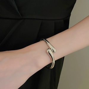 Close-up of a minimalist silver glossy open bangle with an asymmetrical waterdrop design