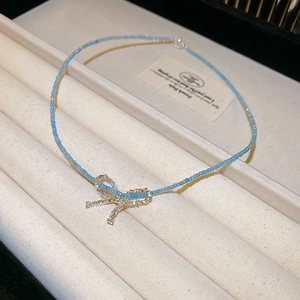 Détail d'un collier en acier plaqué or avec perles bleues et pendentif nœud papillon