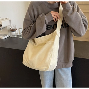 Detail of a large off-white canvas tote bag with front pocket and wide shoulder strap