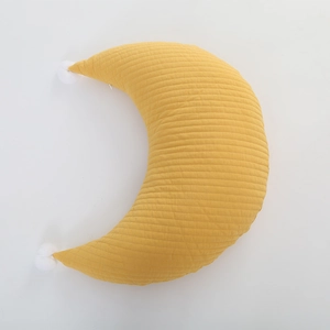 Close-up of yellow moon-shaped nursing pillow with white pom-poms and quilted texture