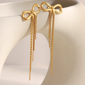 Close-up of 18K gold-plated bow earrings with delicate tassels against a ceramic vase