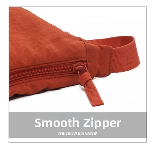 Detail of smooth zipper and reinforced fabric strap on rust red nylon crossbody bag