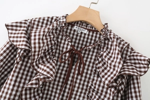 Detail of coffee plaid shirt featuring ruffled collar and adjustable dark drawstring ties
