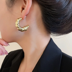 Close-up of golden croissant twist hoop earrings worn by a model in black attire