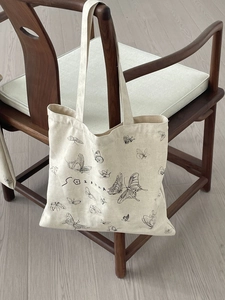 Detailed view of butterfly print on beige canvas tote bag hanging on a wooden chair