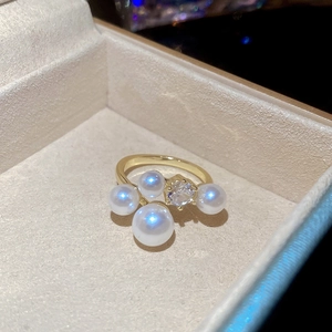 Macro view of gold ring with four white pearls and a clear zircon in a beige jewelry box