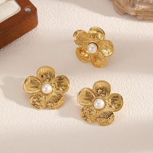 Golden flower earrings set with central pearls and textured metal finish on a neutral surface