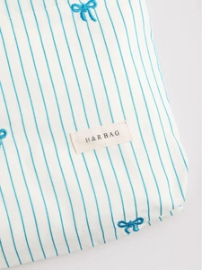 Blue striped fabric cosmetic bag with bow embroidery and branded woven label tag