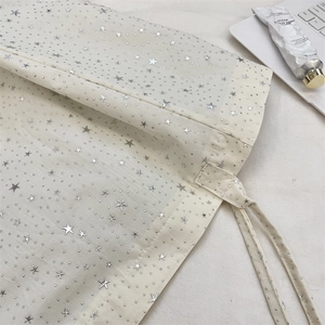 Detailed close-up of white canvas tote bag with shiny silver star patterns and drawstring