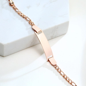 Polished rose gold children's ID bracelet with adjustable Figaro chain on marble