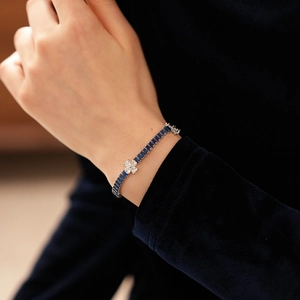 Macro view of blue sapphire rectangular stones and zircon clover charm on silver bracelet