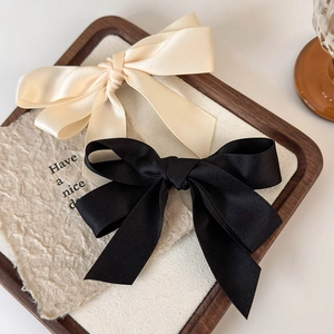 Detail showing two satin bow hair clips in black and beige on a wooden tray