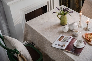 Detail of beige cotton linen tablecloth featuring white daisy prints and tassel fringe edge