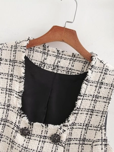 Close-up of black and white tweed vest with fringe trim and decorative dark buttons
