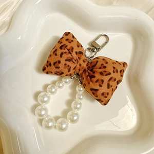 Detail of leopard print fabric bow and white faux pearl keychain on white ceramic plate