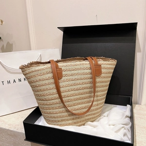 Detail of woven straw beach bag with beige stripes, fringe edge, and brown leather straps