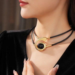 Detail of vintage gold swirl necklace with oval black stone and double leather cord