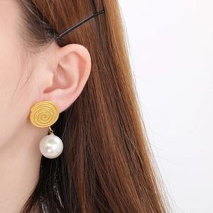 Detail view of gold spiral earring with large white pearl worn by a model