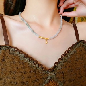 Detail of jade bead necklace featuring a golden bamboo joint pendant on a model