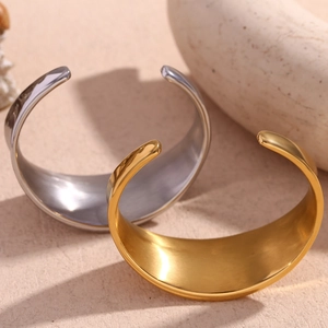 Polished gold and silver concave geometric open bangles set on a minimalist textured surface