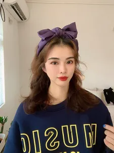 Detail of wide purple satin headband featuring a large 3D bow on a female model