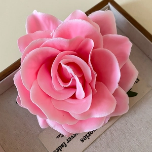 Detailed close-up of a pink fabric rose flower clip and brooch with vintage paper background