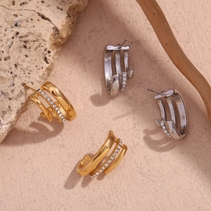 Three-layer C-shaped gold and silver earrings with diamonds on textured stone background