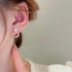 Detail of floral hoop earring featuring white flower, purple crystals, and gold finish