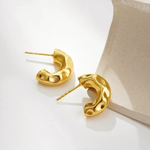 Close-up of gold-plated chunky C-shaped hoop earrings with hammered metal texture design
