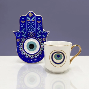 Dettaglio del vassoio Hamsa in ceramica e tazza bianca con motivo malocchio e bordi dorati