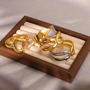 Macro detail of minimalist gold and silver spring cuff bracelets on wood tray