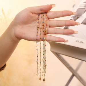 Detail of gold stainless steel cross bracelets with colorful beads held by hand