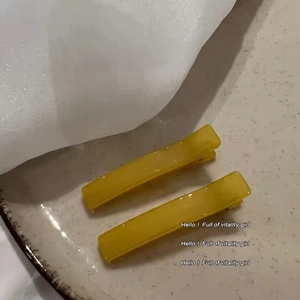 Close-up of two yellow rectangular duckbill hair clips with marbled texture on ceramic plate
