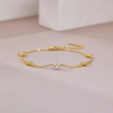 Detailed macro view of a gold-tone floral charm bracelet with sparkling zircon accents