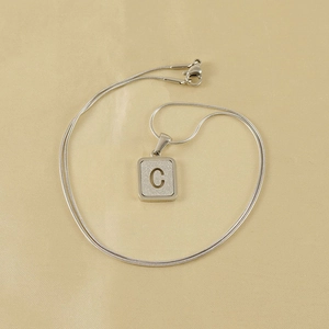 Detail of silver snake chain necklace featuring a frosted square pendant with letter C