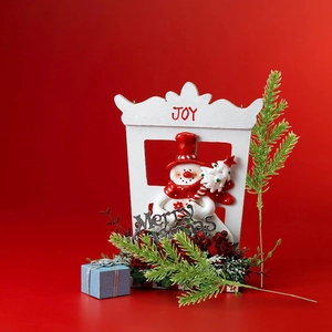 Christmas snowman decor in a white frame with festive greenery and a red backdrop