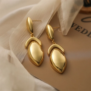Detailed view of gold plated teardrop tassel earrings on elegant cream fabric