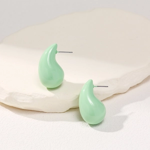 Macro detail of mint green teardrop stud earrings on a textured white stone surface