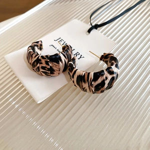 Macro shot of C-shaped leopard print resin earrings on a white jewelry card with glass