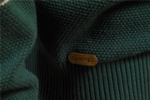 Detail of dark green waffle knit sweater featuring a brown leather brand tag at the hem