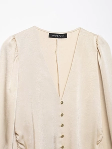 Détail d'un chemisier en satin champagne avec col en V, boutons dorés et texture plissée
