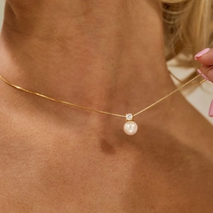 Close-up of gold box chain necklace with white pearl and zircon pendant on model