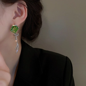 Detail of green square gemstone earrings with silver tassel on a model in a black suit