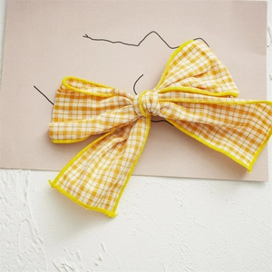 Detail of yellow and white checkered fabric bow hair clip on a minimalist art card