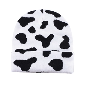 Detail of warm knit beanie featuring a black and white cow print with a ribbed cuff edge